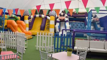 An indoor play area with inflatable slides and a fenced play zone.