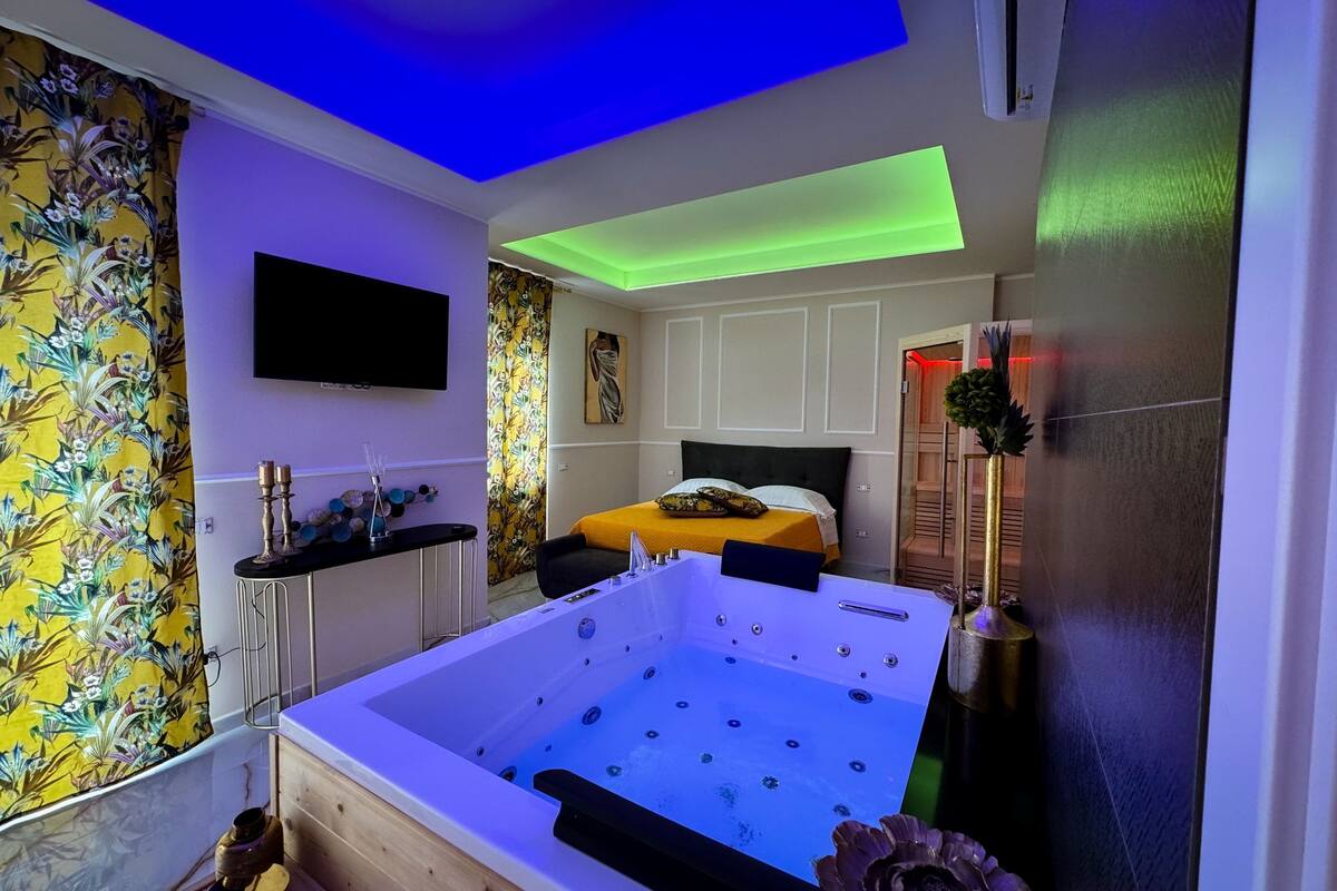 Un dormitorio moderno con una bañera grande, un televisor de pantalla plana y una cama con colcha amarilla.