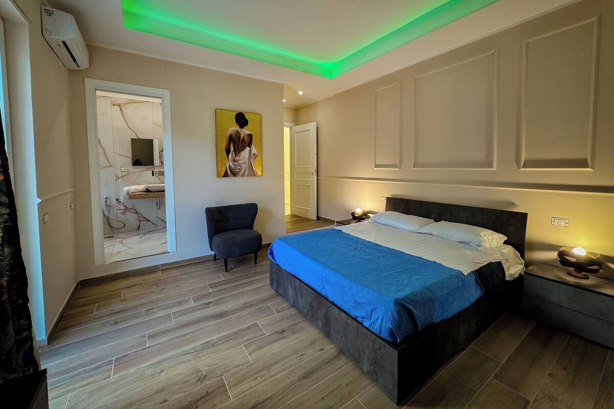 Un dormitorio moderno con cama, una silla y un baño visible a través de una puerta abierta.
