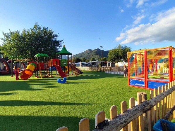 A playground with various play structures, a fenced area, and a mountain in the background. - Dream Room (Mercato San Severino)