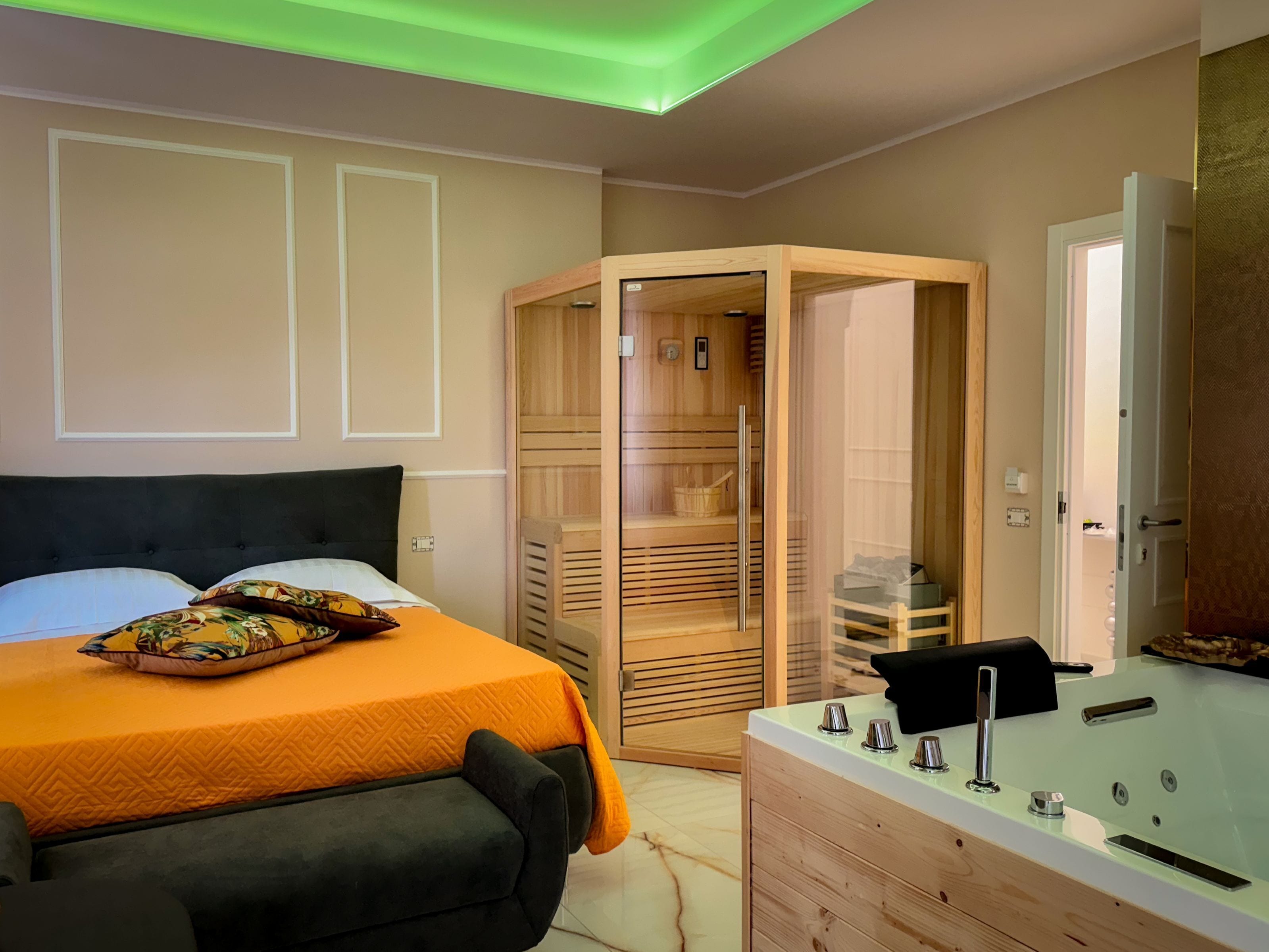 A bedroom with a bed, a wooden wardrobe, a glass-enclosed sauna, and a bathroom with a bathtub.