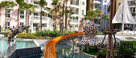 A pool area with a dolphin-shaped slide and a polka-dotted sculpture.