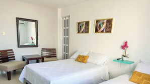 A hotel room with two beds, a desk, a chair, a mirror, and artwork on the wall. - CASA VERANO SAN ANDRES (San Andrés)