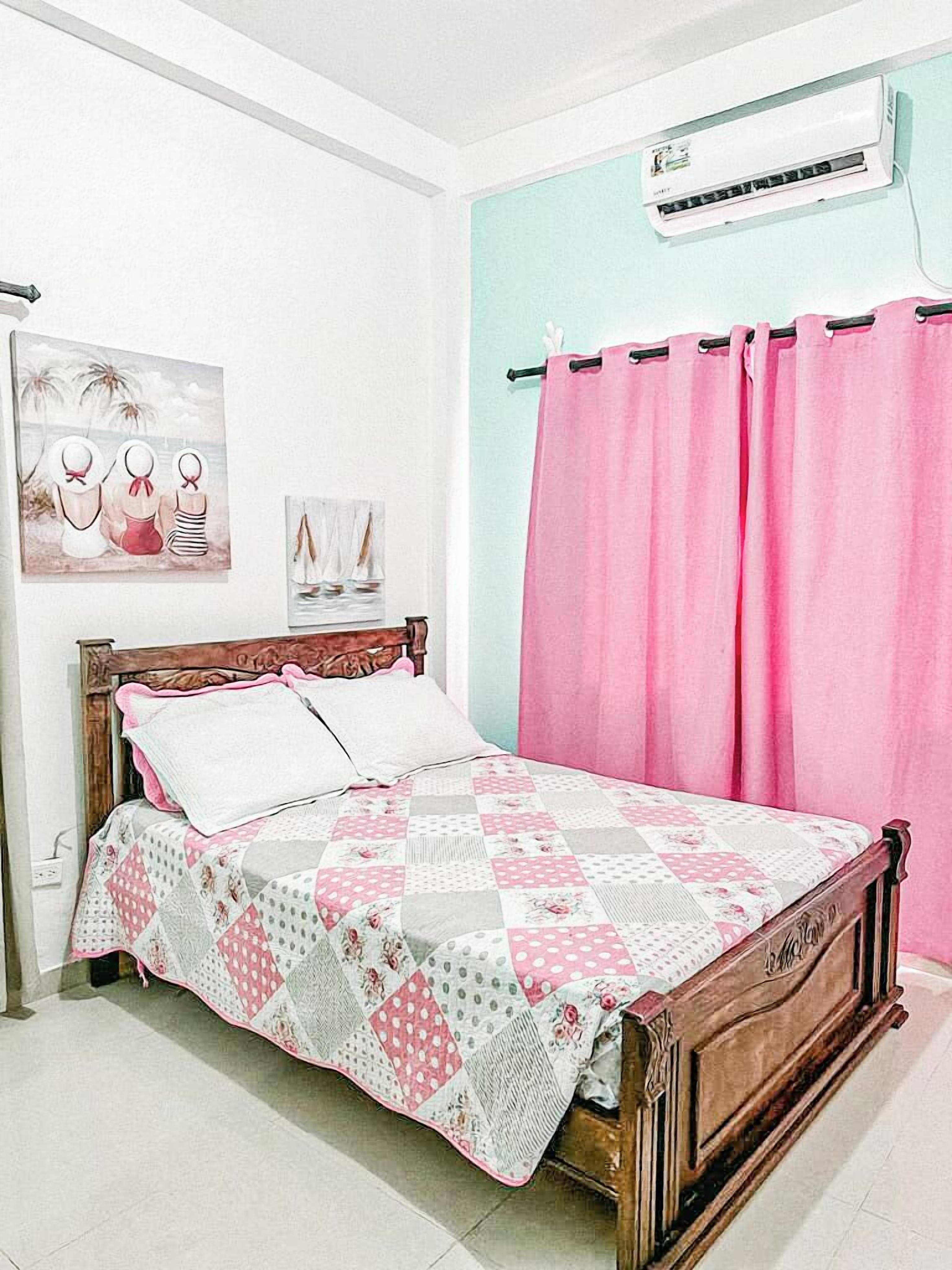 Een slaapkamer met een houten bed, roze gordijnen en een gewatteerde spreideken.