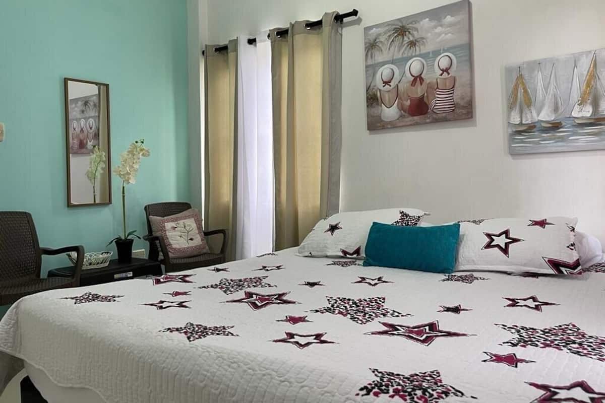 Un dormitorio con una cama, dos sillas, una planta en maceta y dos cuadros en la pared.