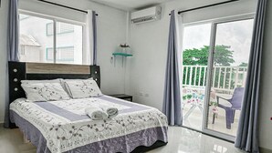 A bedroom with a bed, a nightstand, a window, and a balcony with chairs. - CASA VERANO SAN ANDRES (San Andrés)