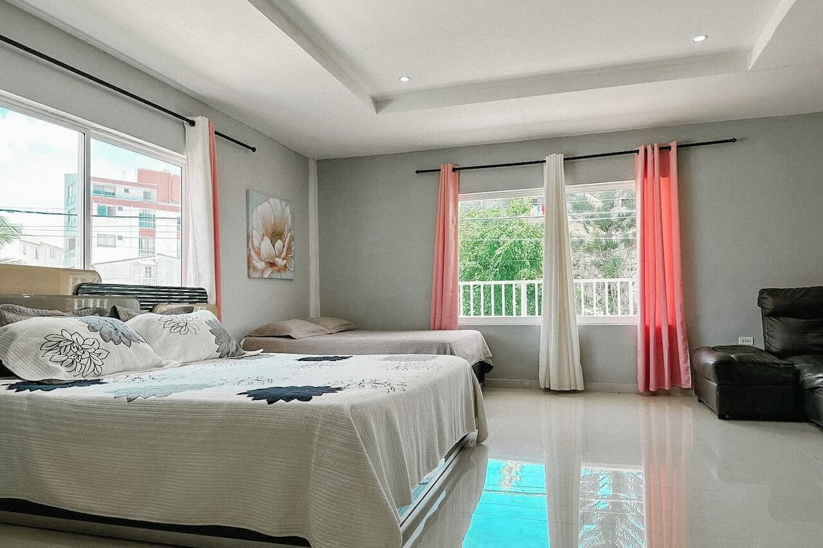 Un dormitorio moderno con dos camas, un sofá y un balcón con cortinas.