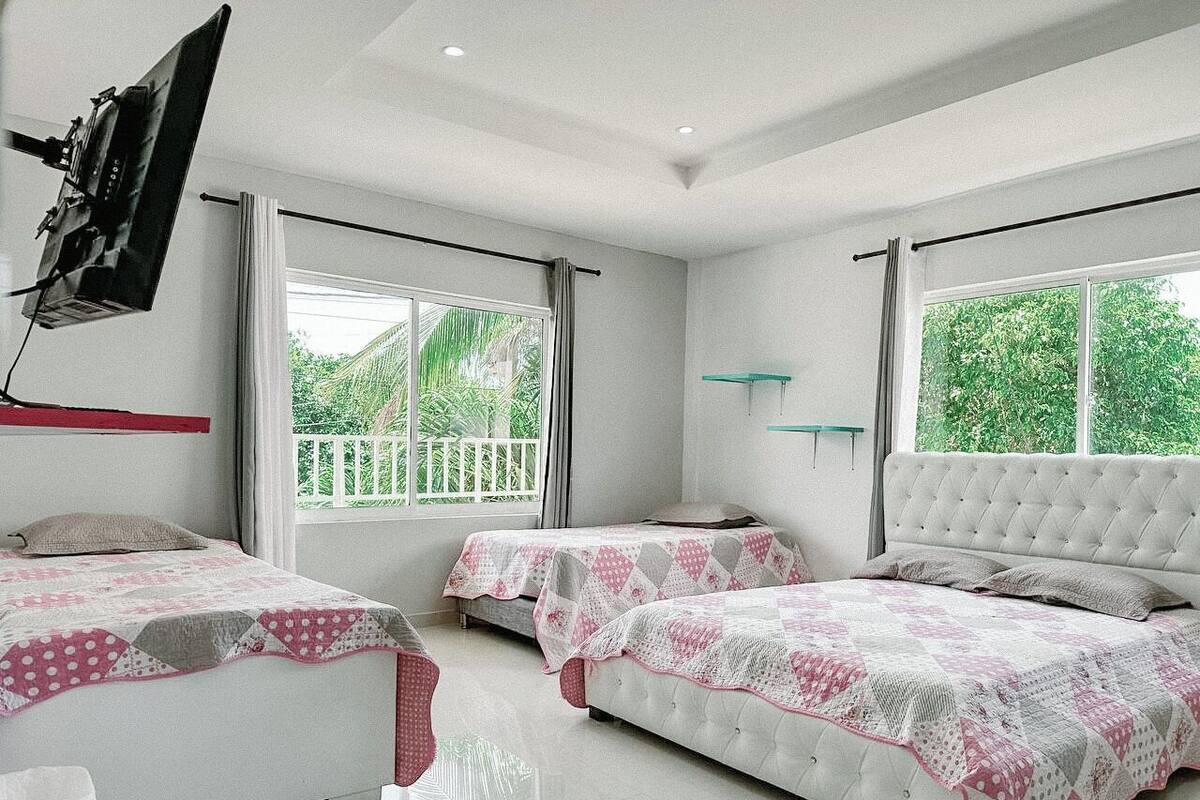 Un dormitorio con dos camas, ventanas amplias, un televisor de pantalla plana en la pared y un balcón.