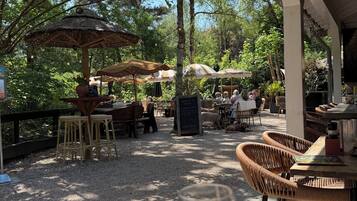An outdoor seating area with wicker furniture, a glass of white wine, and a thatched umbrella.