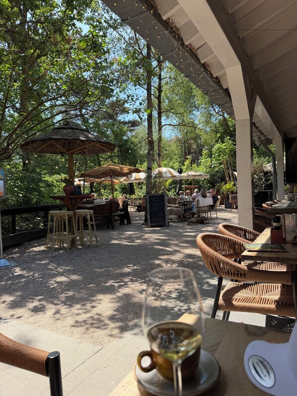 Un espacio al aire libre con mobiliario de mimbre, una copa de vino blanco y un paraguas de paja.
