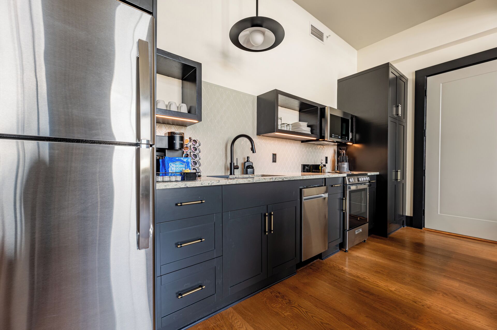 A modern kitchen with stainless steel appliances, dark cabinetry, and a wooden floor.