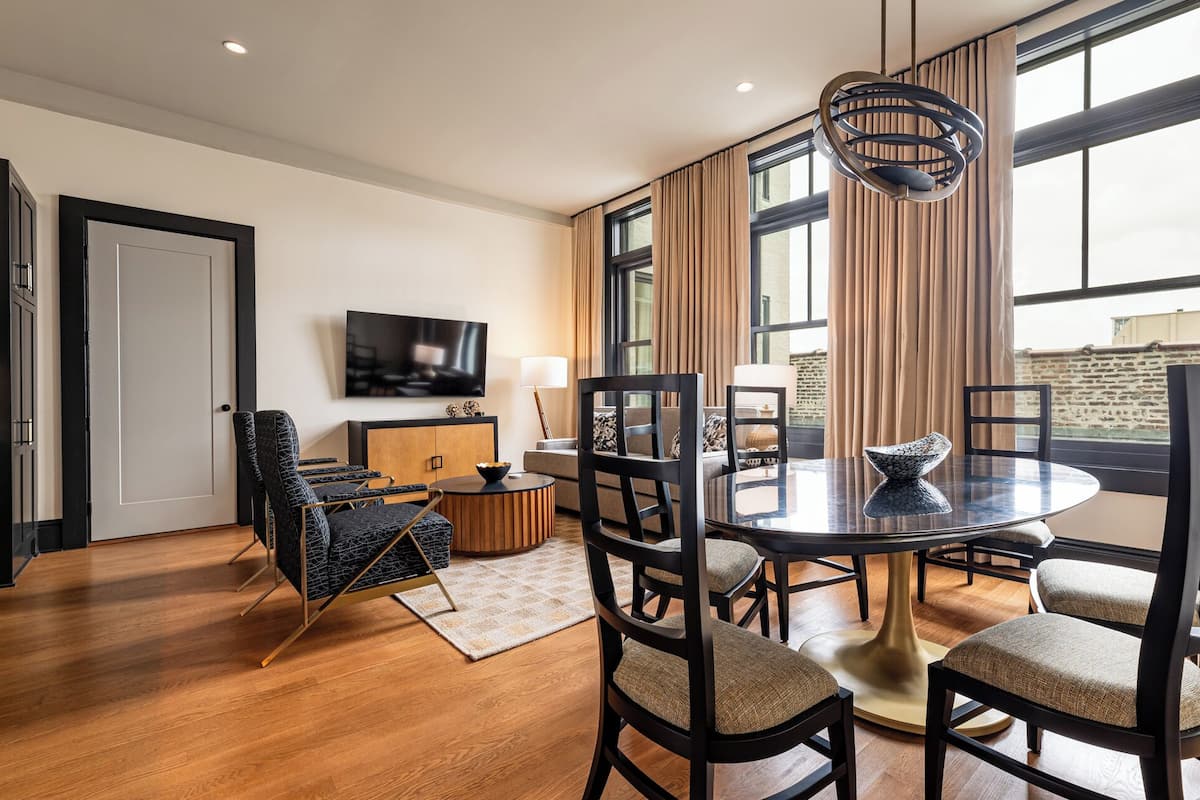 A modern dining area with a round table, six chairs, and a television mounted on the wall.