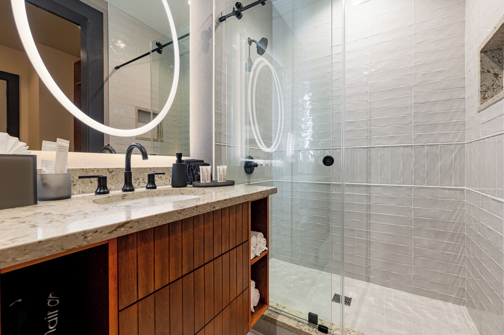A modern bathroom with a marble countertop, a black faucet, and a glass-enclosed shower area.