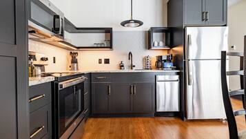 A modern kitchen with dark cabinetry, stainless steel appliances, and a wooden floor.
