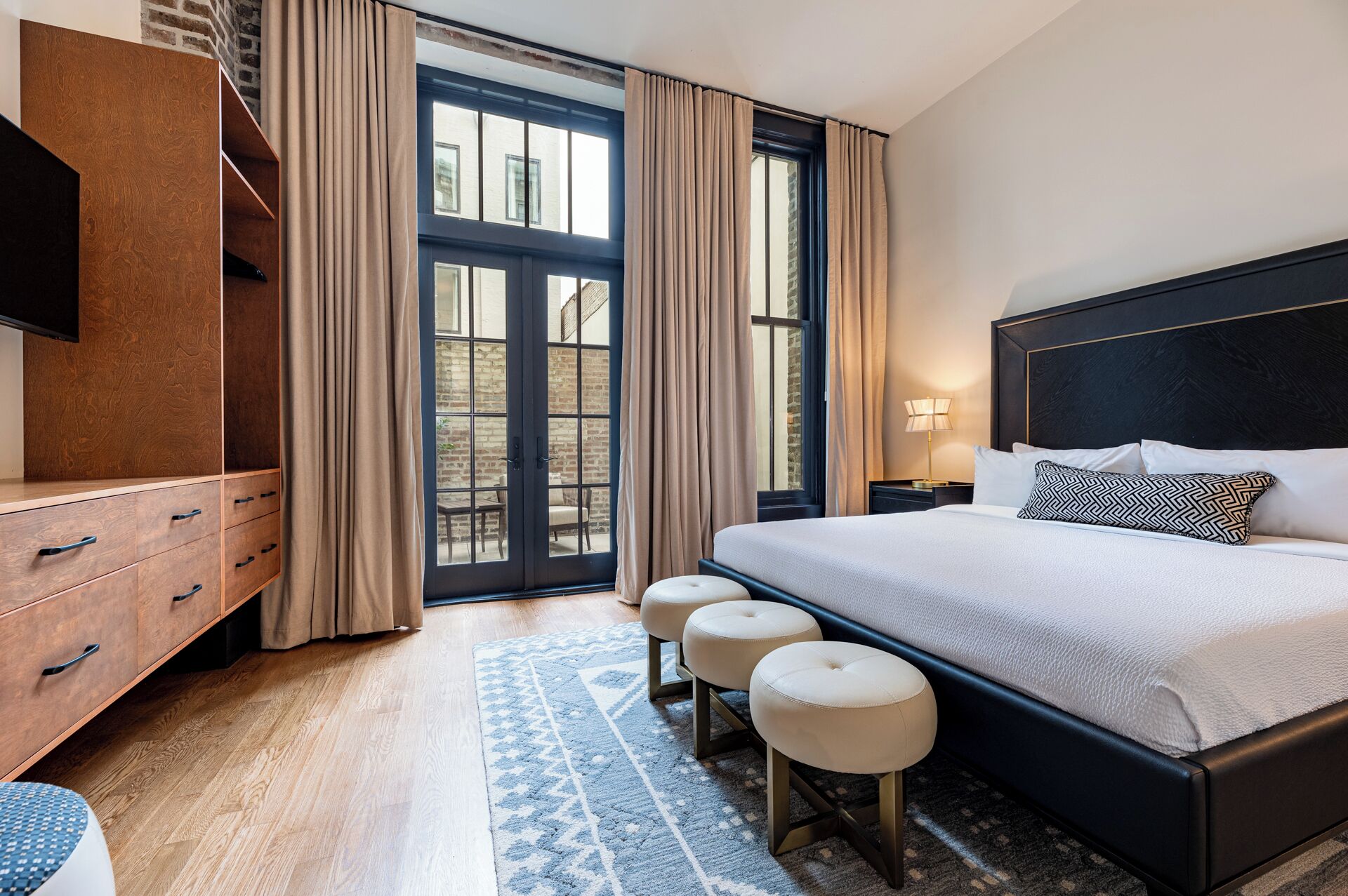 Une chambre d’hôtel moderne avec un grand lit, une commode en bois, une télévision et une vue sur l’extérieur grâce à une porte vitrée.