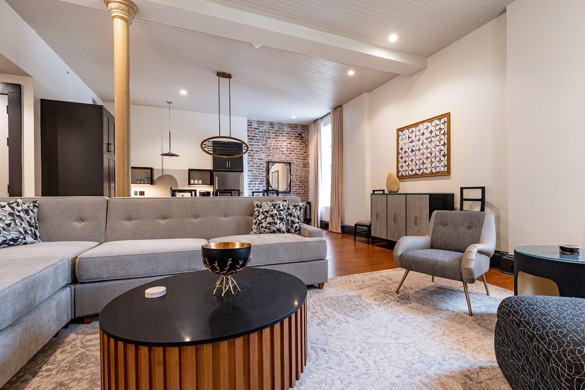 A modern living room with a grey sofa, a round black coffee table, and a grey armchair.