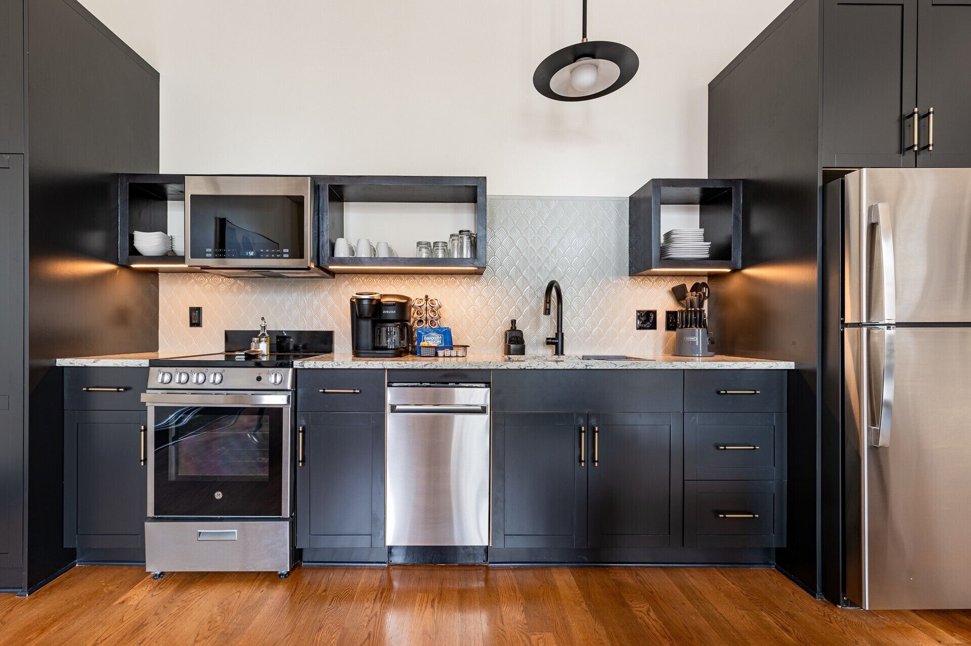 Cozinha moderna com eletrodomésticos de aço inoxidável, armários pretos e painel de fundo decorado.