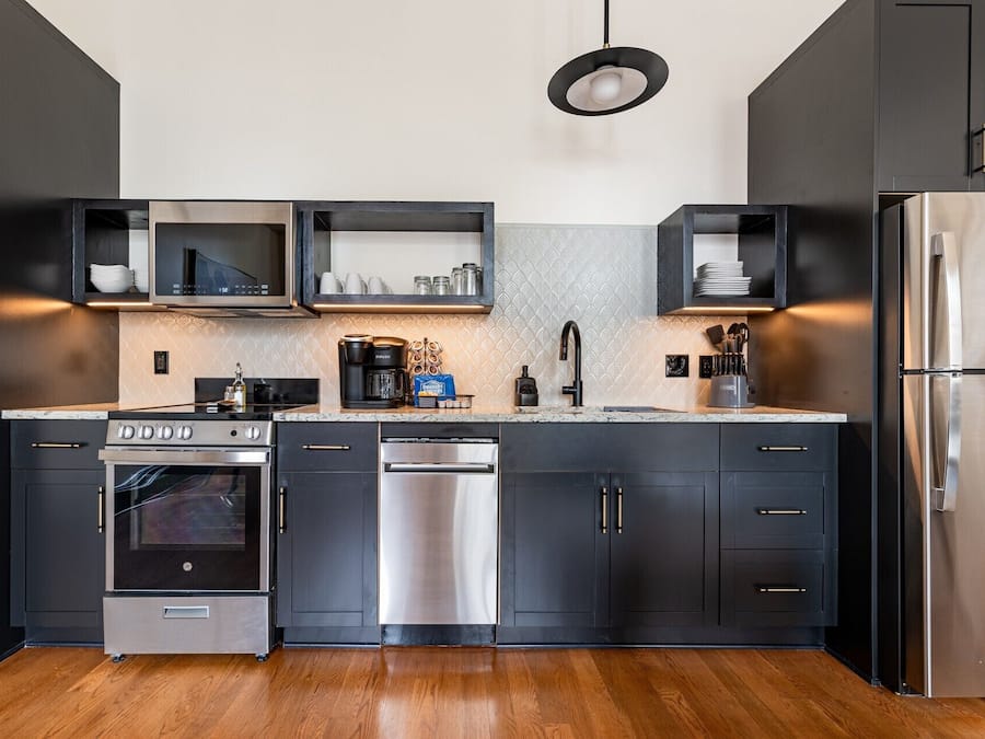 A modern kitchen with stainless steel appliances, black cabinetry, and a patterned backsplash.