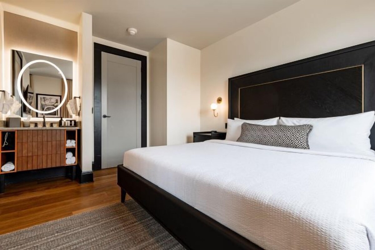 A bedroom with a large bed, a vanity with a mirror, and a door.
