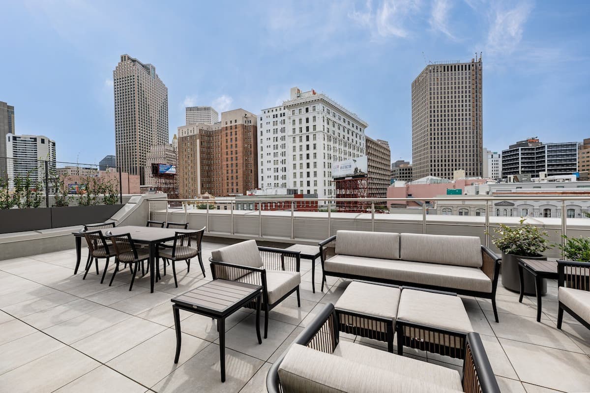 A rooftop terrace with outdoor furniture, including tables and sofas, overlooking a cityscape with various buildings.