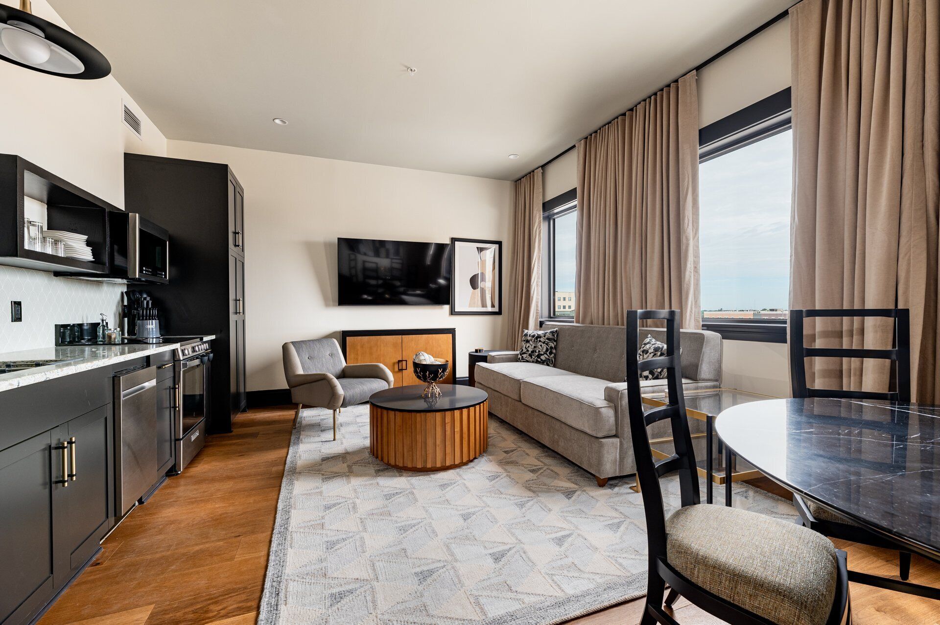 Een moderne hotelkamer met een keuken, een bank, een eettafel en een groot raam.