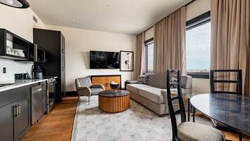 Una habitación de hotel moderna con cocina, sofá, mesa de comedor y un ventanal grande.