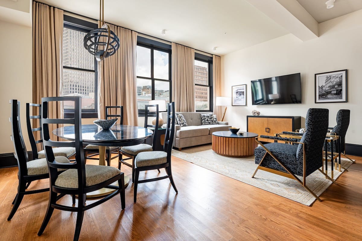 A modern living room with a dining area, large windows, a flat-screen TV, and a city view.