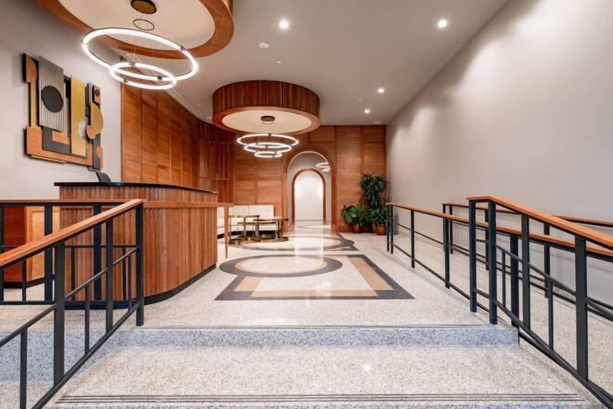 A modern hotel lobby with a reception desk, wooden paneling, a marble floor, and a staircase.
