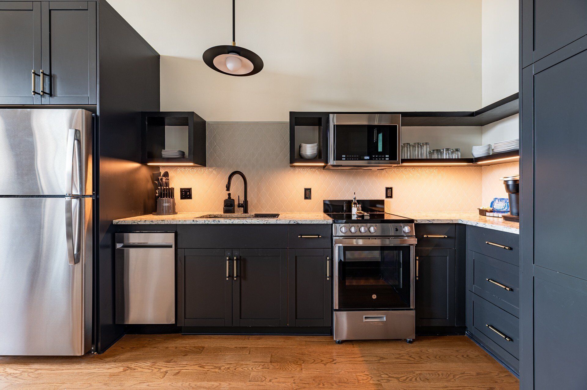 Una cocina moderna con armarios oscuros, electrodomésticos de acero inoxidable y suelo de madera.
