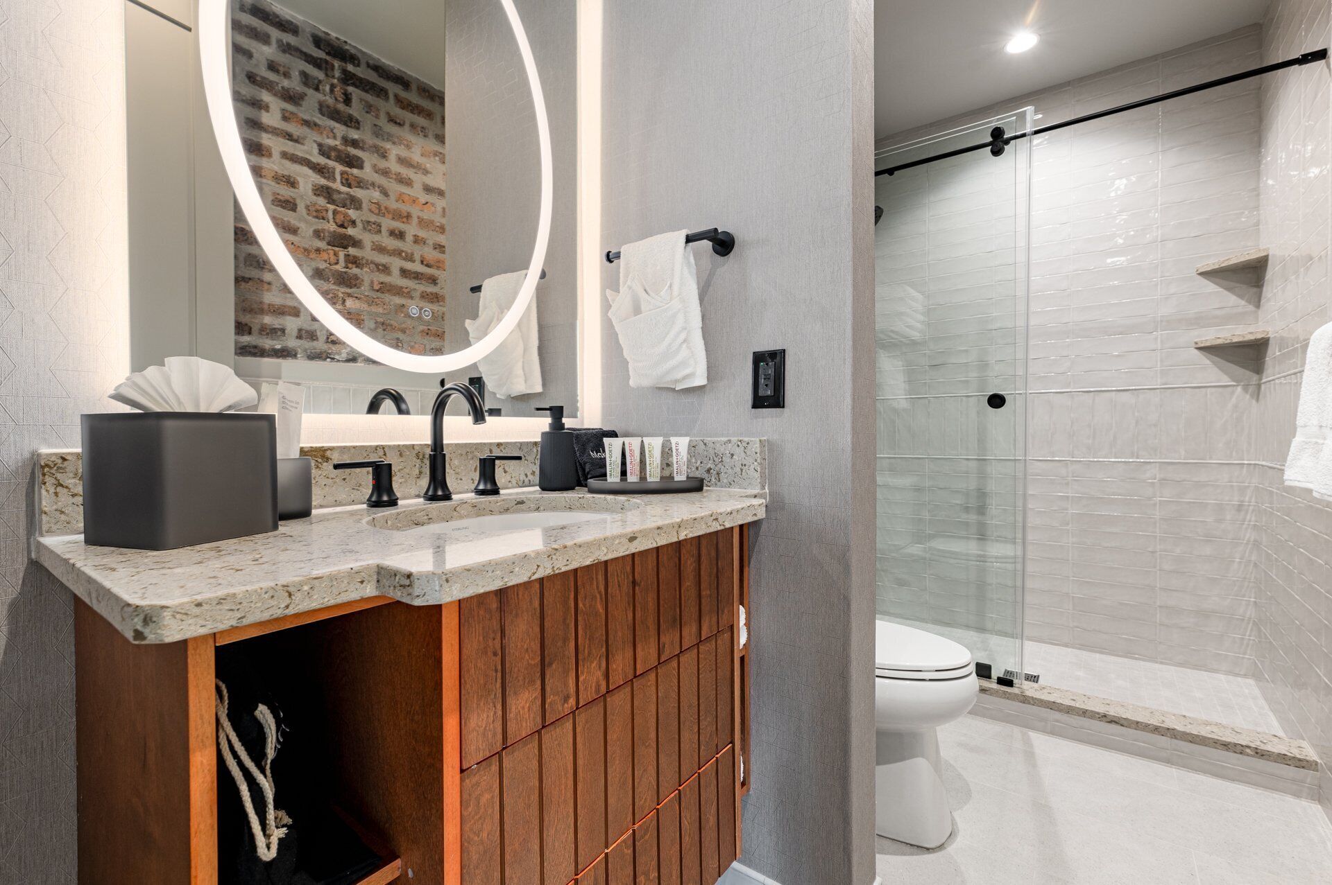 A modern bathroom with a granite countertop, a wooden vanity, a large mirror, and a glass-enclosed shower.