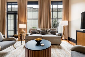 A modern living room with a sofa, two side chairs, a coffee table, and a TV. - The Mayfair (New Orleans)