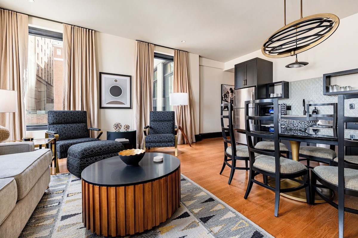 A modern living room with a sofa, two armchairs, a coffee table, and a dining area with chairs and a table.
