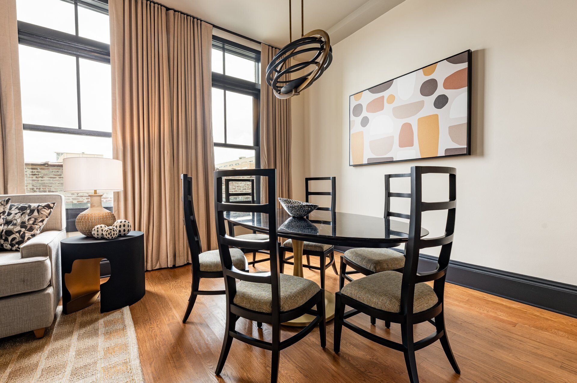 A modern living room with a round dining table, four chairs, a sofa, a lamp, and a large abstract painting on the wall.