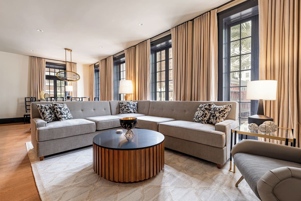 A modern living room with a sectional sofa, a round coffee table, and large windows with curtains.