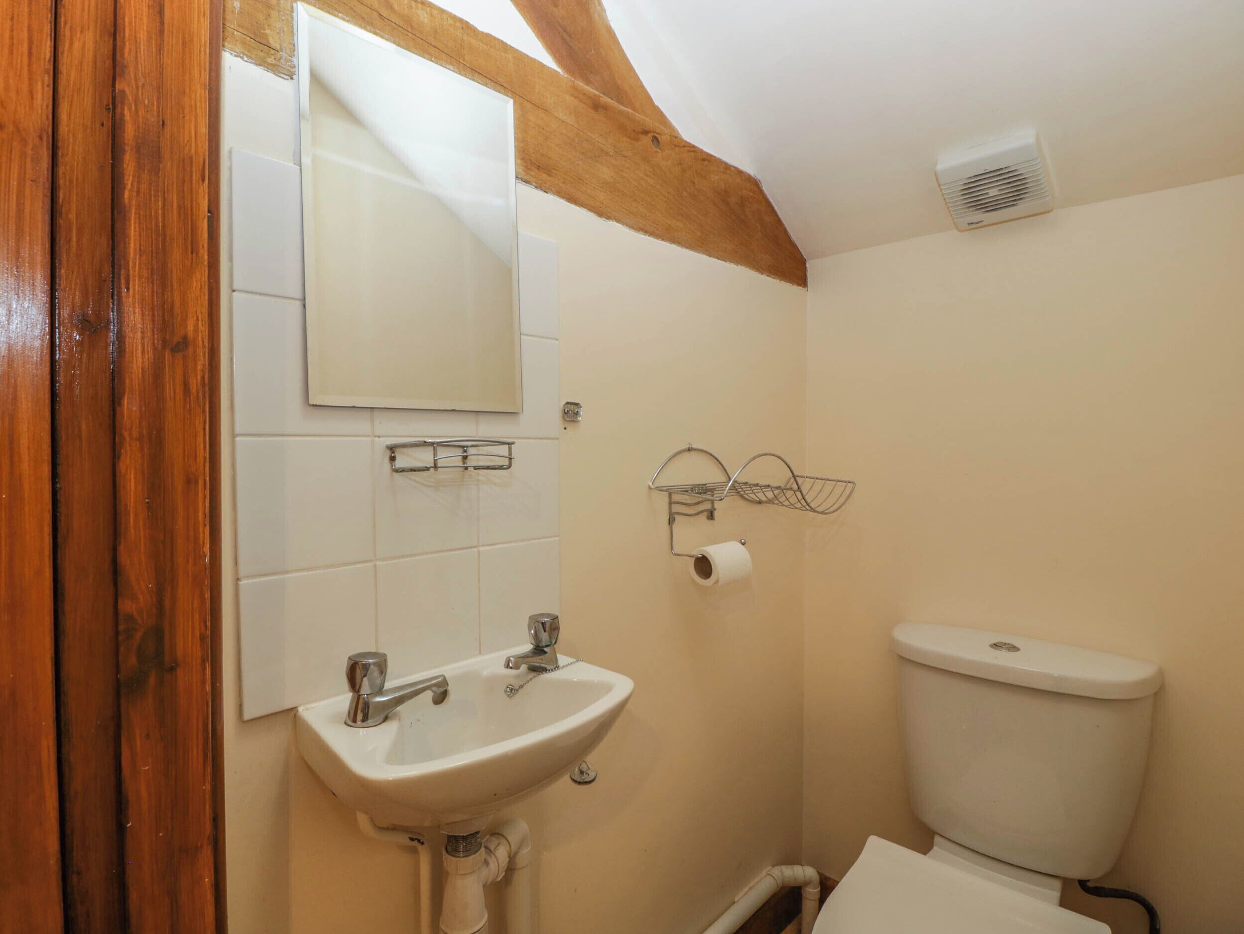Ein Badezimmer mit weißem Waschbecken, Spiegel, Toilette und einem Holzbalken an der Decke.