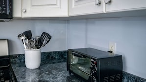 A kitchen with a black toaster oven, a white utensil holder, and a marble countertop. - Coastal Haven in West Dennis -15 (West Dennis)