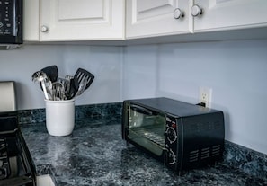 A kitchen with a black toaster oven, a white utensil holder, and a marble countertop. - Coastal Haven in West Dennis -15 (West Dennis)