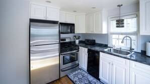A modern kitchen with white cabinets, stainless steel appliances, and a granite countertop. - Coastal Haven in West Dennis -15 (West Dennis)