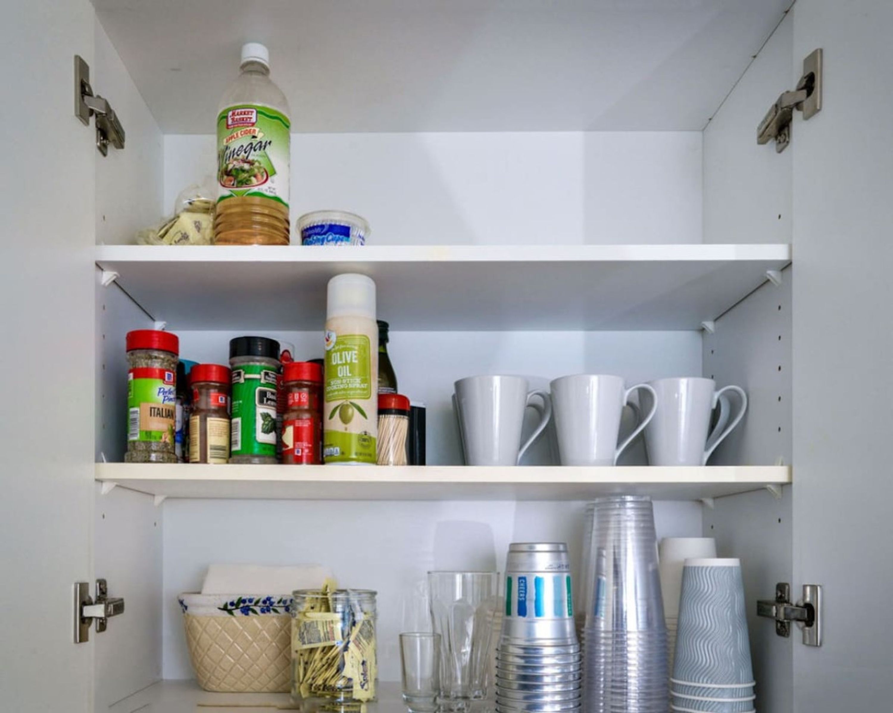 Een provisiekast met planken vol met diverse levensmiddelen, waaronder kruiden, olijfolie en sauzen.