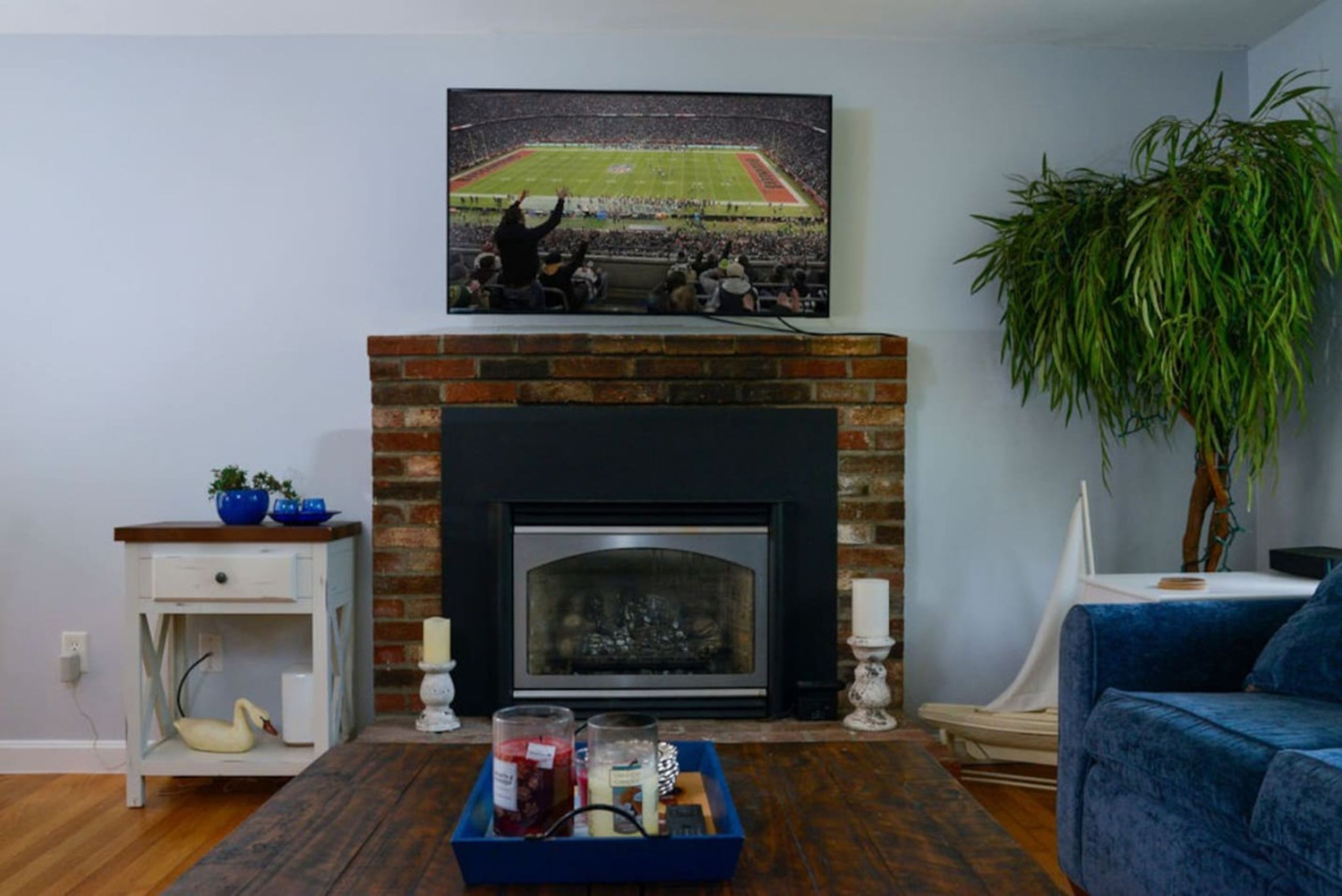A living room with a fireplace, a television mounted above it, a blue sofa, and a potted plant.