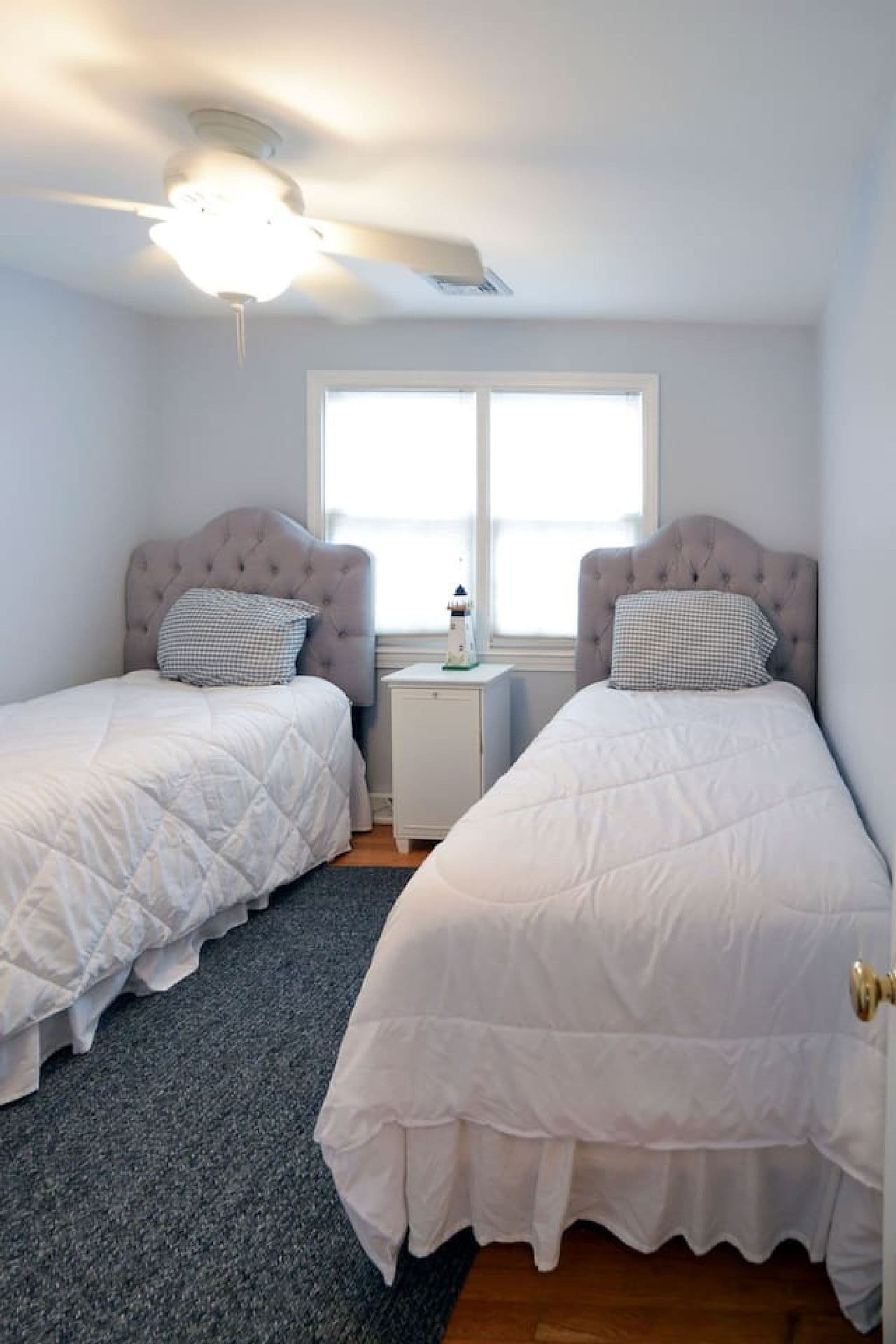 Ein Schlafzimmer mit zwei Betten, einem Deckenventilator, einem Fenster und einem Nachttisch mit einer Lampe.