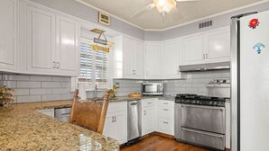 A kitchen with white cabinets, a granite countertop, a microwave, a stove, and a refrigerator. - Coastal Charm Lobster Ch Teau (Swampscott)