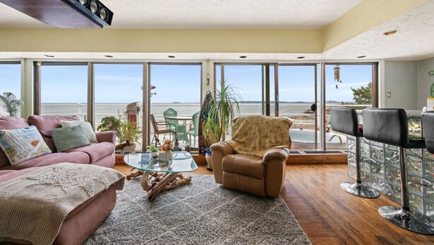 A spacious living room with a large window overlooking the sea, a comfortable sofa, a glass coffee table, and a leather armchair. - Coastal Charm Lobster Ch Teau (Swampscott)