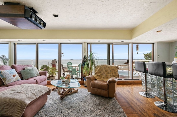 Un salon spacieux avec une grande fenêtre donnant sur la mer, un canapé confortable, une table basse en verre et un fauteuil en cuir.