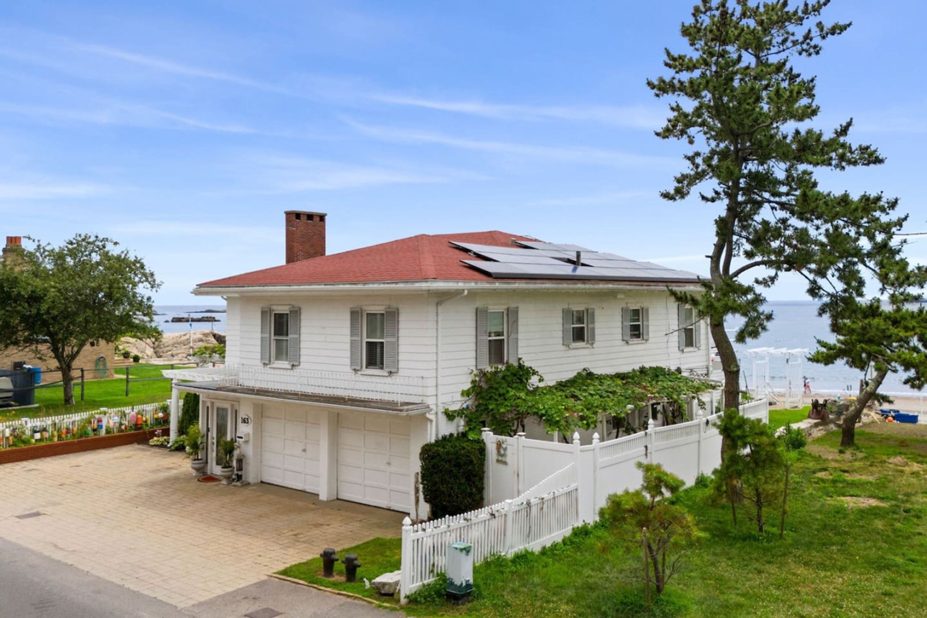 A white two-story house with a red roof, a garage, and a view of the ocean.