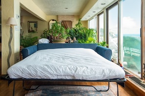 A bedroom with a bed, a view of the ocean, and several potted plants. - Coastal Charm Lobster Ch Teau (Swampscott)