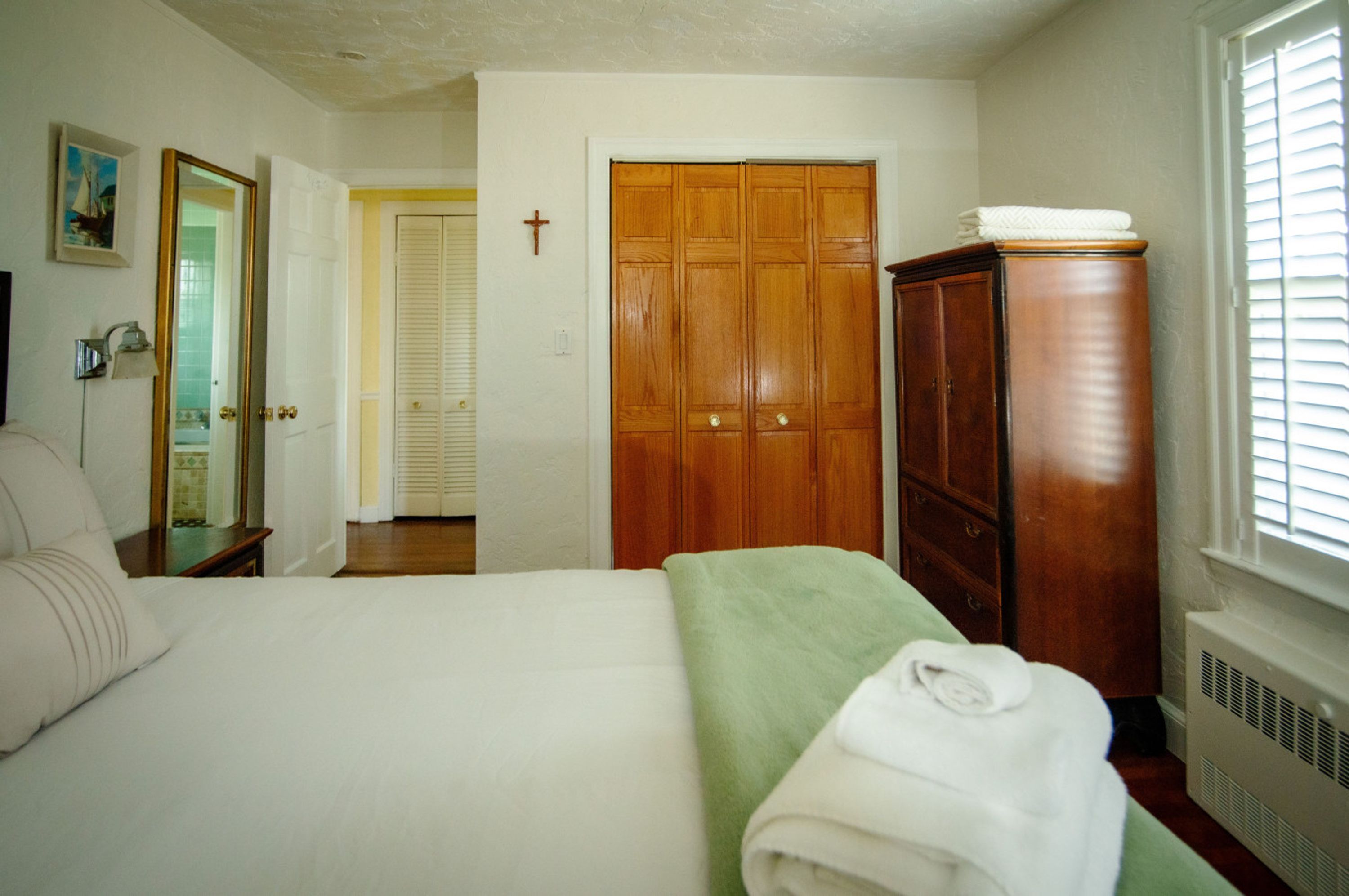 Un dormitorio con cama, armario, espejo y una cruz en la pared.