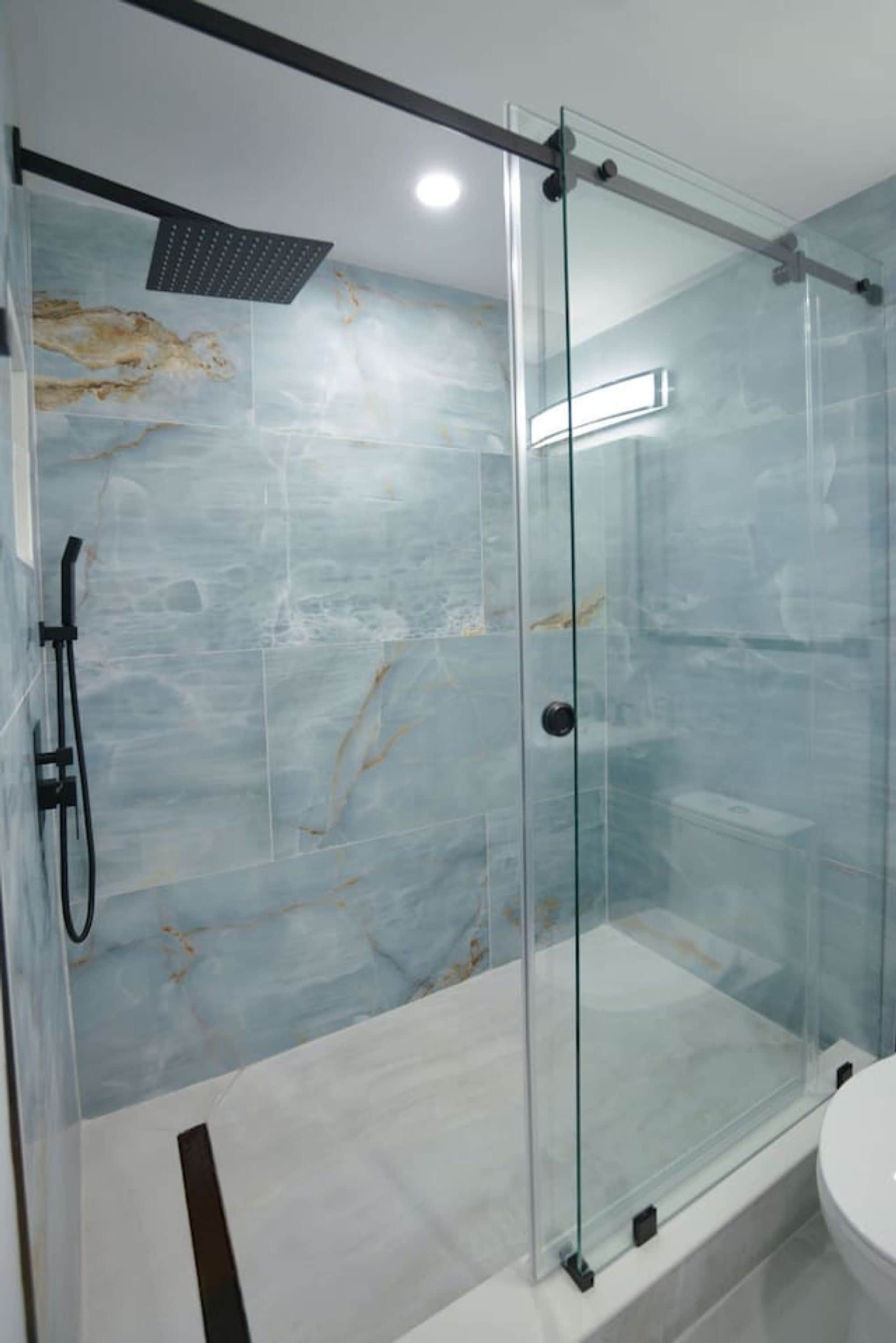 Une salle de bain moderne avec une douche en verre, des murs en marbre et un lavabo blanc.