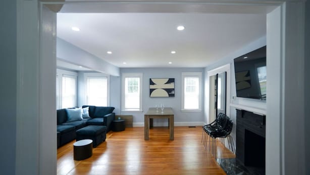 A spacious living room with a wooden floor, a dark-colored sofa, a small round table, and a fireplace. - Enchanting Hidden Door Escape (Stoneham)