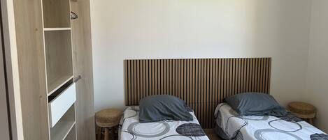 Ein Schlafzimmer mit zwei Einzelbetten, einem Holzschrank, einem gewobenen Hocker und einer Pendelleuchte.